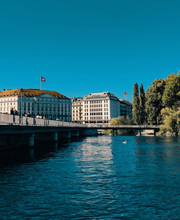 Capture of a serene urban waterfront in Geneva with historic buildings and clear blue skies.