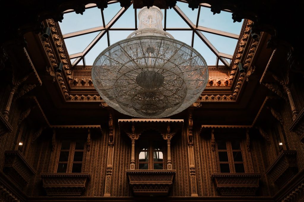 Lavish chandelier hanging inside an intricately decorated atrium with a glass ceiling.